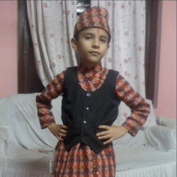 Young Amrit Raj Pokhrel, around 5–7 years old, wearing traditional Nepali Doura Surwal with Dhaka Topi, smiling at the camera.

